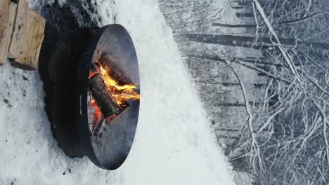 Vertikaler-Schuss-Feuer-In-Schüssel-In-Ländlicher-Verschneiter-Szene,-In-Der-Nähe-Von-Gefrorenen-Bäumen-Im-Winter