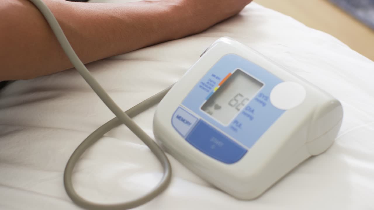 Braccio di adulto appoggiato sul letto mentre un monitor della pressione sanguigna misura dopo il simbolo di avvio, registrando le letture, con spazio per il testo.