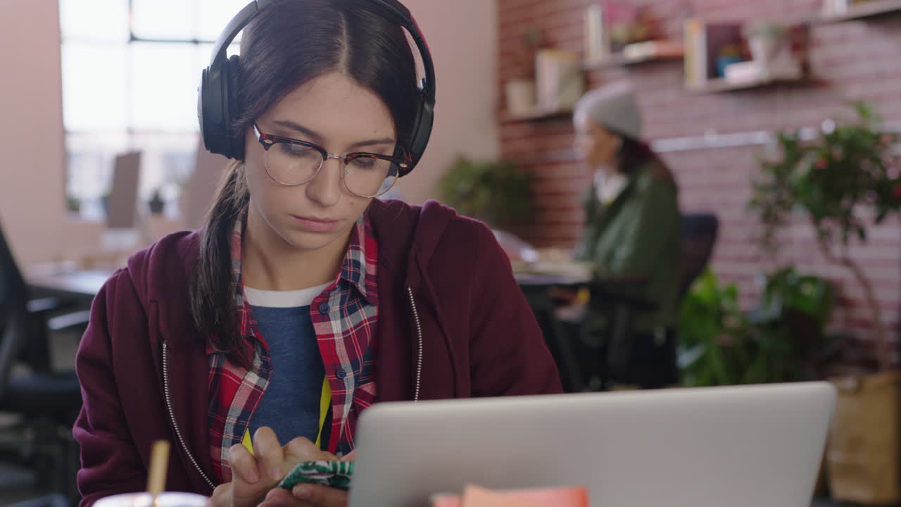 hermosa mujer de negocios caucásica pasante usando computadora portátil escribiendo navegando mensajes en línea bebiendo jugo escuchando música revisando teléfono inteligente en una oficina moderna y de moda