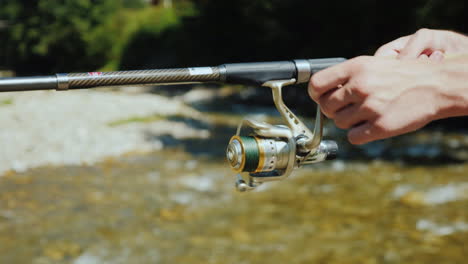 manos de pescador con pesca giratoria cerca de un pequeño río de montaña