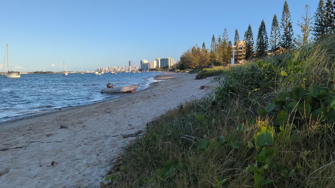 Pan up, beach grass with the city, boat and beach in the background.