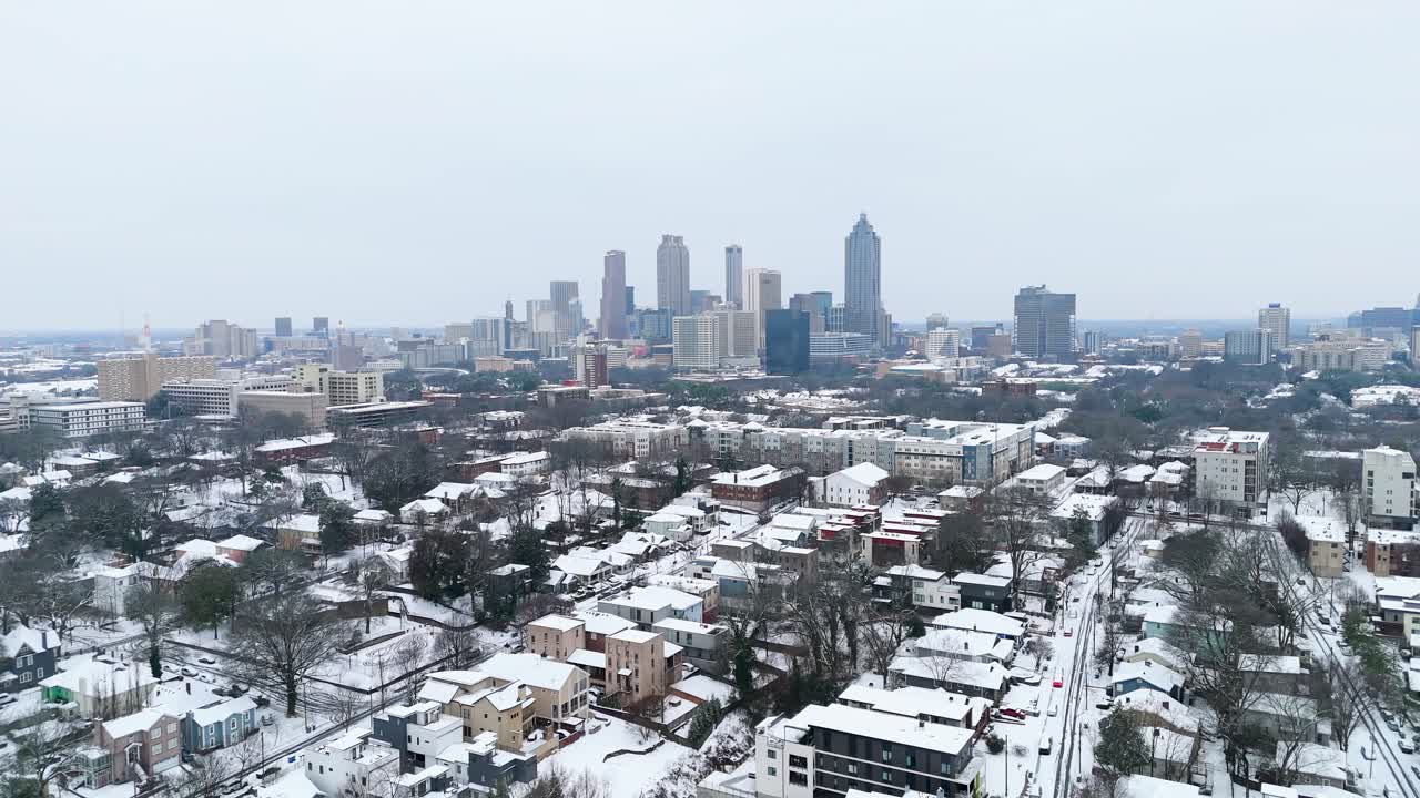 Aerial push in on the snow covered suburbs of Midtown Atlanta Georgia with skyscrapers in the background.