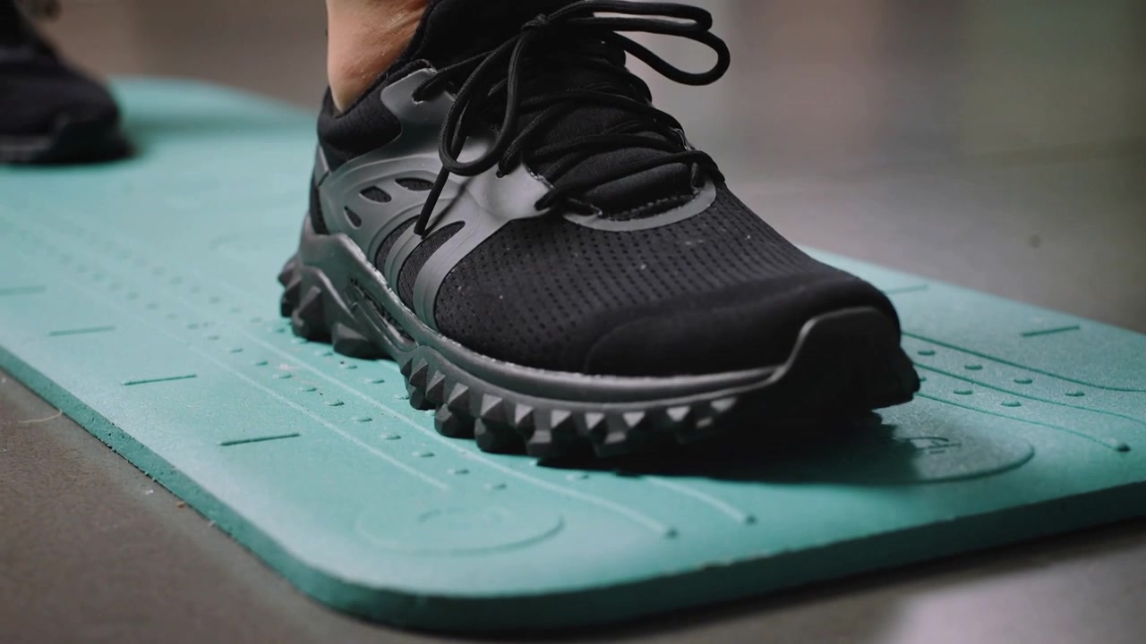 Appoggiando il piede destro con una scarpa da ginnastica nera su un tappetino color verde acqua nella stanza, spostando il peso dalla scarpa sinistra.