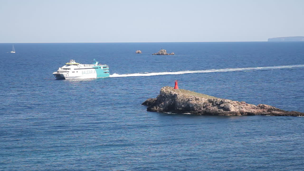 Ferry sailing near a rocky island with a red lighthouse