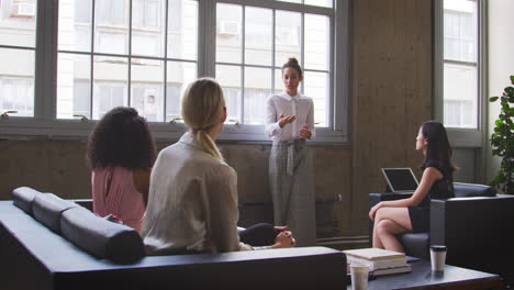 Businesswoman-stands-to-address-colleagues-at-casual-meeting