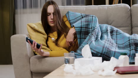 tired girl with thermometer using smartphone