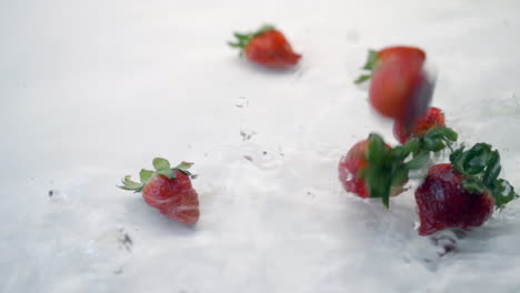 slomo of strawberries falling into water on white backdrop