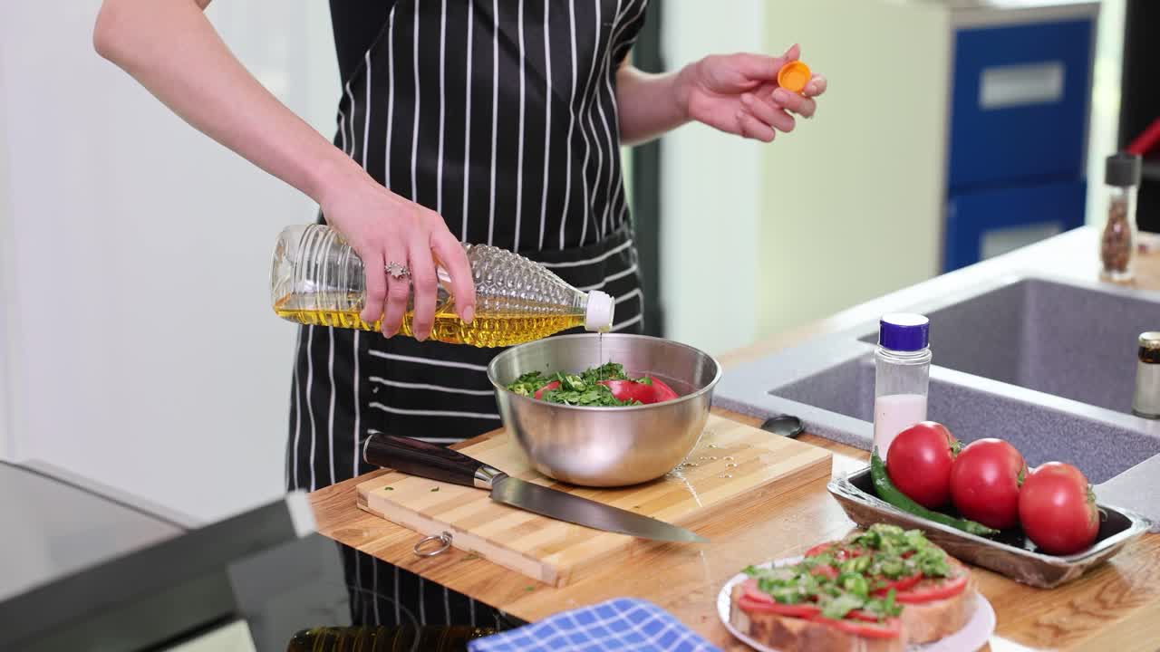 Person preparing food by pouring oil into a bowl of vegetables