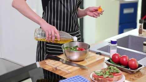 person preparing food by pouring oil into a bowl of vegetables