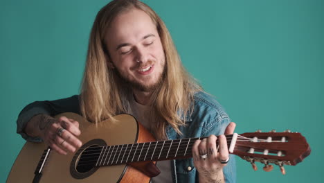 un joven caucásico tocando la guitarra y cantando ante la cámara.