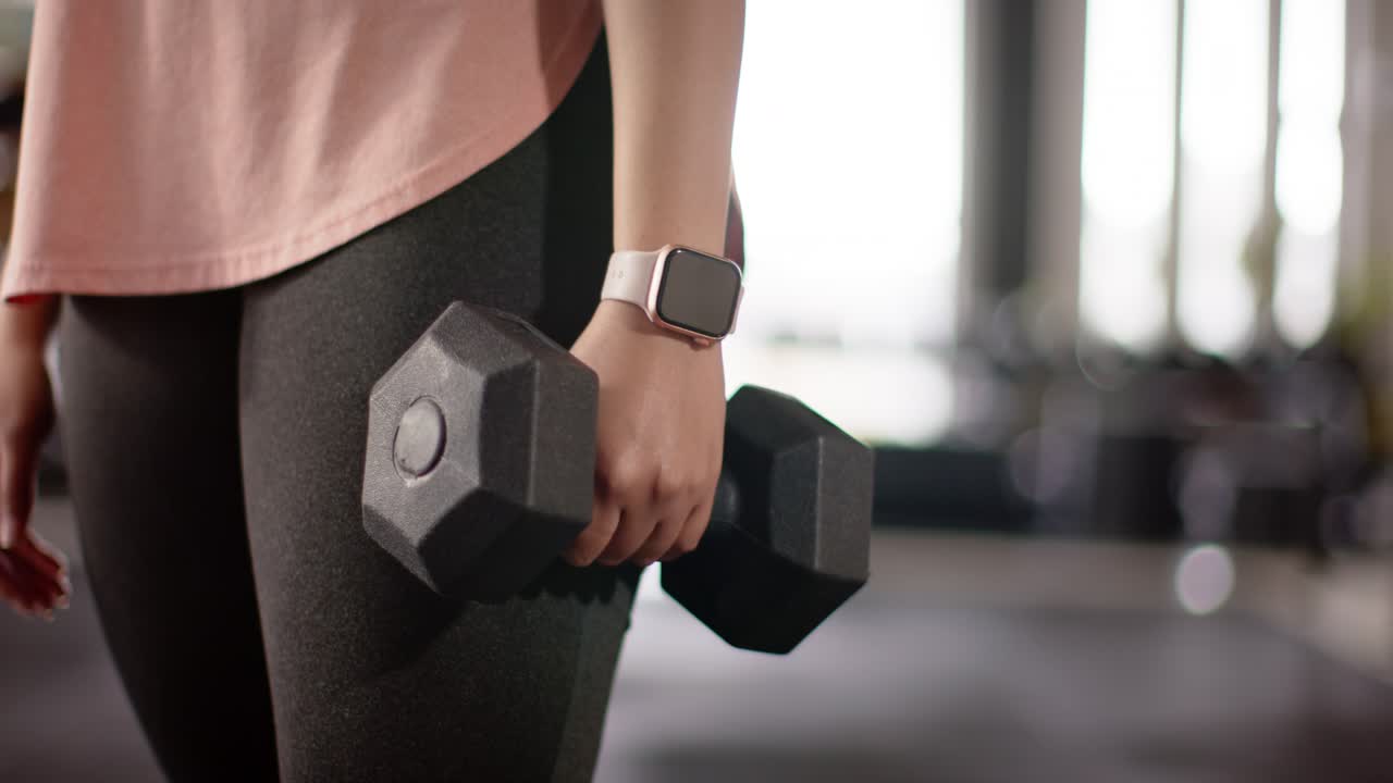 User's right hand is grasping dumbbell as light streaming through studio windows for muscle toning