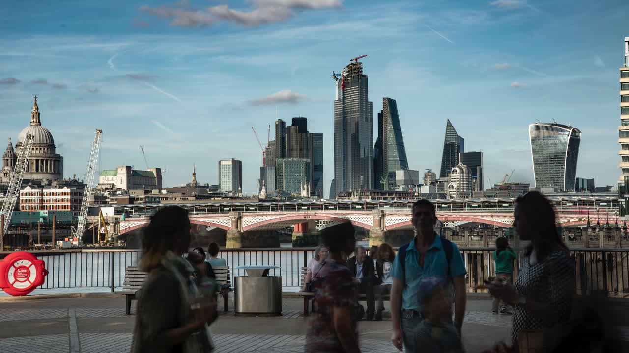 Blurred tourists in London fill the foreground of this time lapse, with the city skyline in the background, viewed from the south bank of the River Thames
