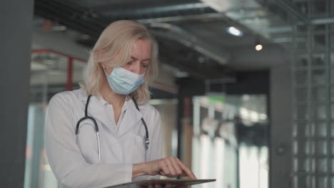 a blonde, middle aged female doctor in a facemask consults data on a tablet