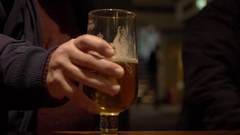 man's hand with glass of beer in a bar close up shot