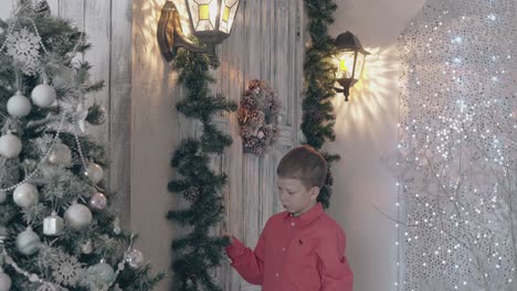 schoolboy in red shirt touches pine garland decor in room