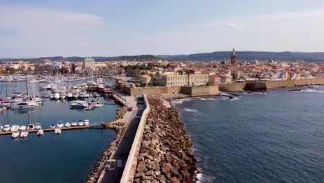 clip de drones de un lujoso puerto deportivo con yates y un rompeolas fuera de los muros del castillo de la ciudad de alghero en cerdeña, italia