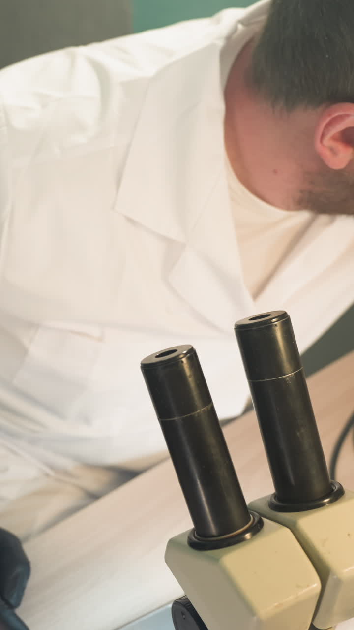 현미경을 통해 전자 부품을 검사하는 데 초점을 맞춘 실험실 코트를 입은 기술자의 클로즈업 뷰