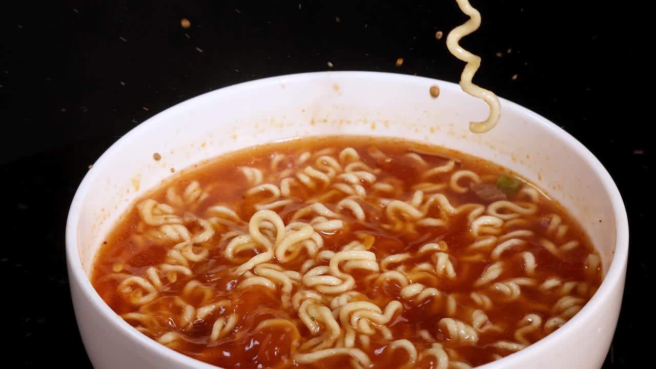 Cooked instant noodles are released from chopsticks into a bowl of hot broth. Close-up shots, dark background, and steady camera highlight the action