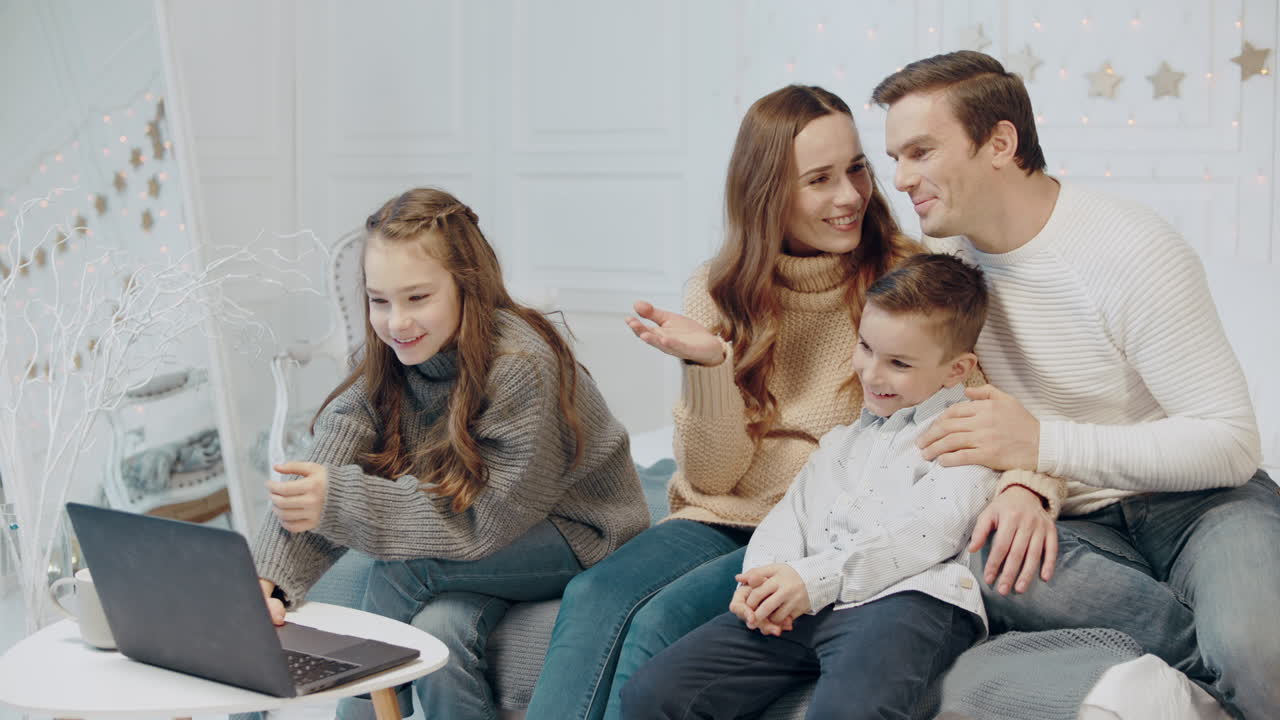 улыбающаяся семья вместе смотрит видео на ноутбуке в гостиной.