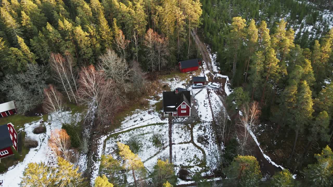 Drone slowly flying towards a remote red cabin in a large Swedish forest