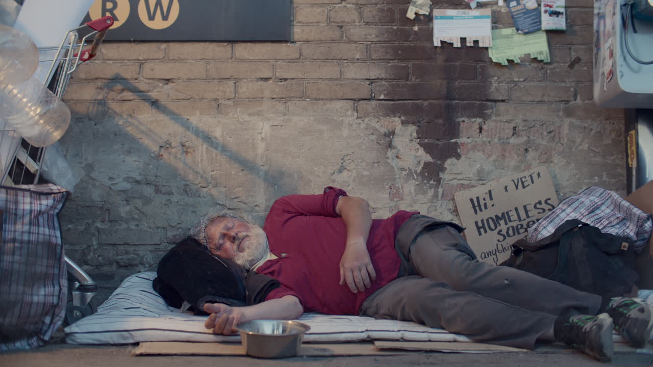 Senior Homeless Man Sleeping on Sidewalk as Pedestrians Donating Money to Him