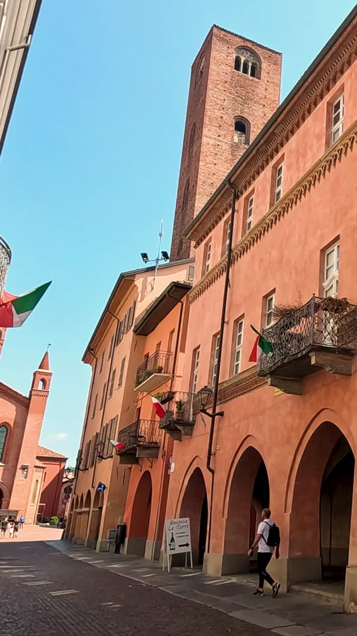 Una vista verticale di un edificio storico in mattoni rossi con portici ad arco e bandiere.