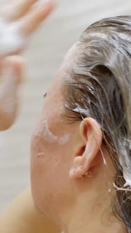 blonde girl washes her hair. white foam from shampoo on long hair. head hair care. vertical video