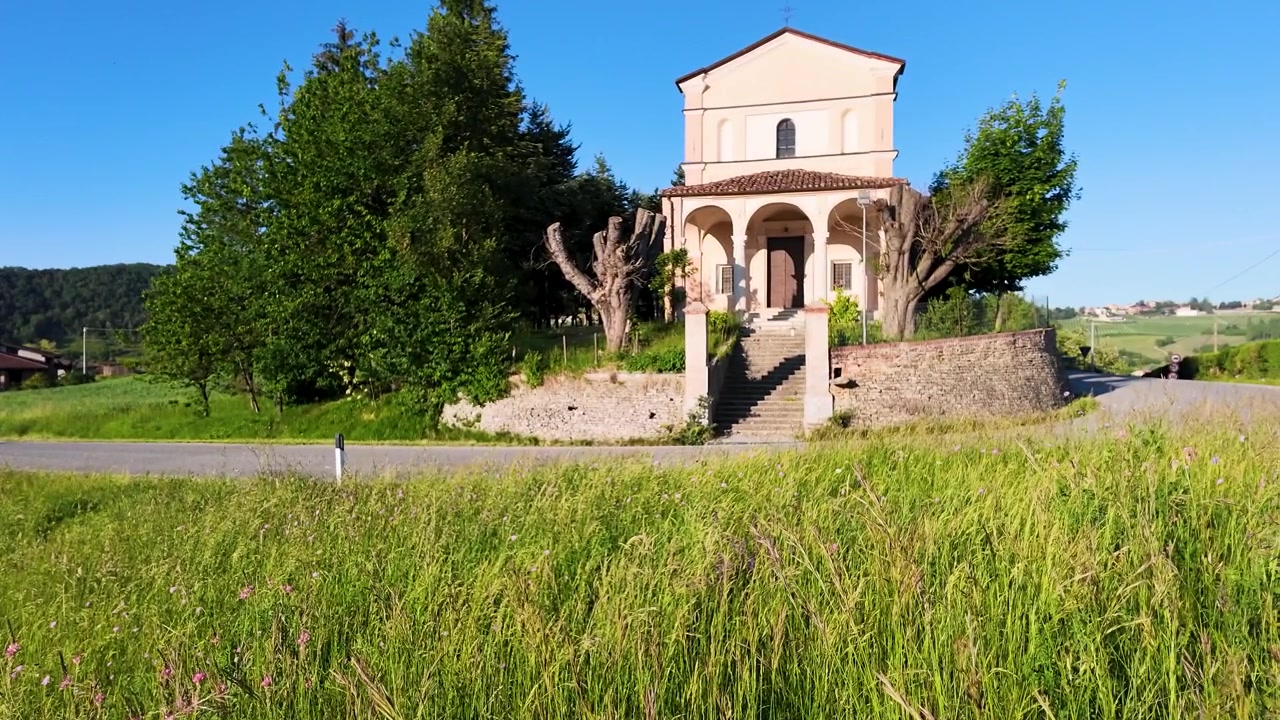 Una telecamera dal basso si alza attraverso l'erba alta e verde verso una chiesa rurale soleggiata.