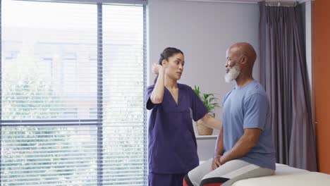 Diverse-female-physiotherapist-and-senior-male-patient-in-hospital-physical-therapy-session-on-neck