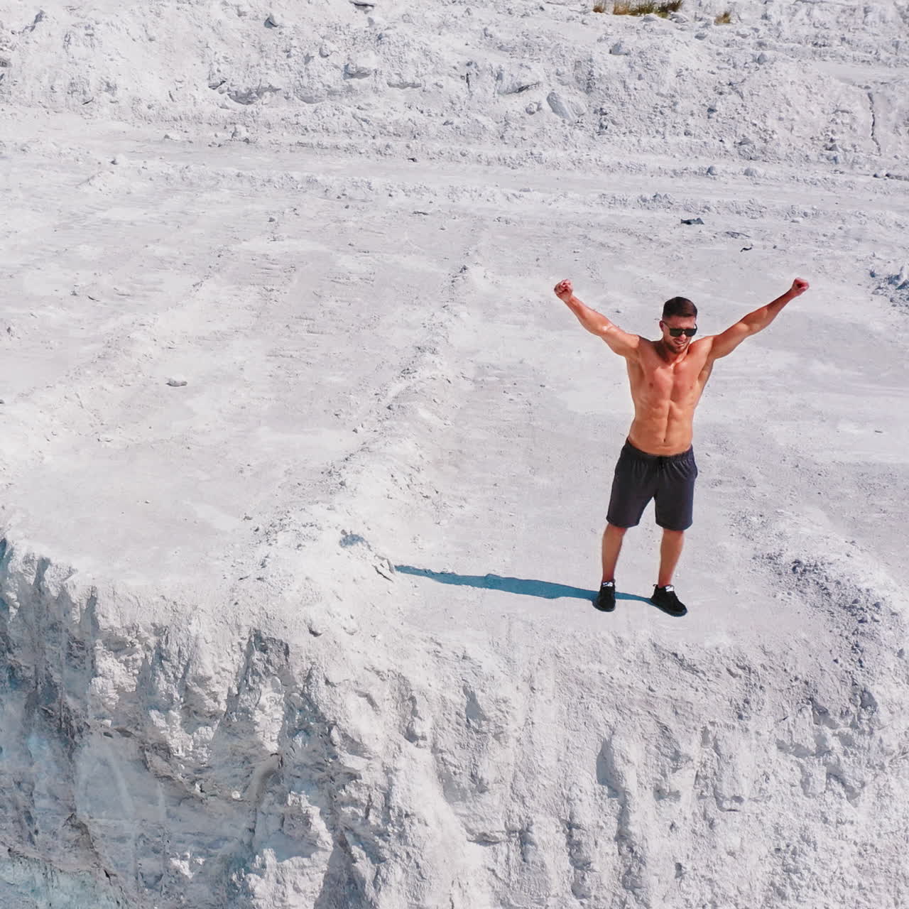 Healthy man running on white canyon. Shirtless athlete training happily on beautiful natural background in summertime. Aerial view.