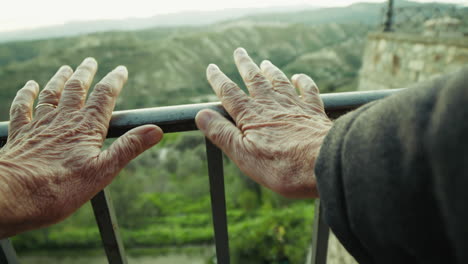 point of view hands of an elderly gentleman cling to a railing overlook nature