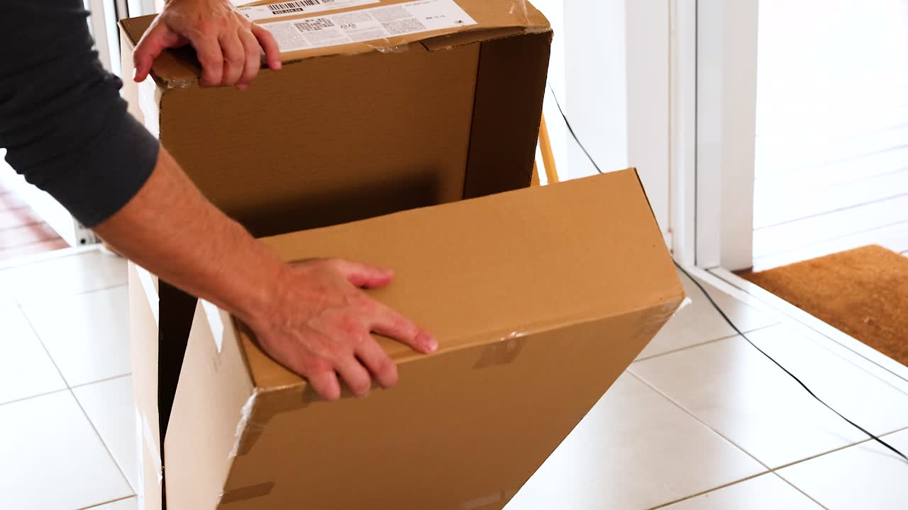 A person opens a cardboard box, revealing wooden slats inside, in a well-lit indoor setting