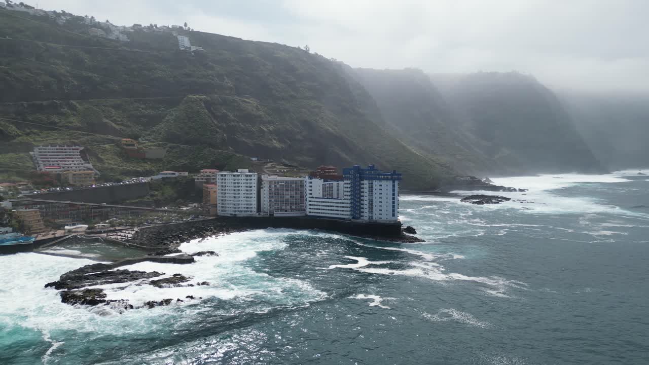 Piscinas naturais de água do mar de Mesa del Mar com edifícios de apartamentos para aluguel em Tenerife, Ilhas Canárias, Espanha, tomada aérea com panorâmica para a direita