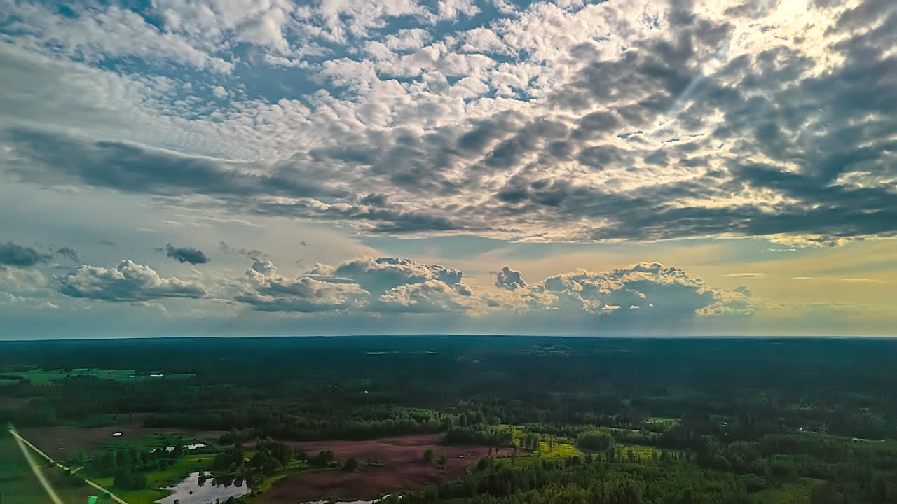 Stunning aerial hyperlapse flies over vast Latvian landscape with green forests, lakes, and agricultural fields as dramatic clouds move across the sky