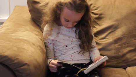 little girl reading a book alone on the couch