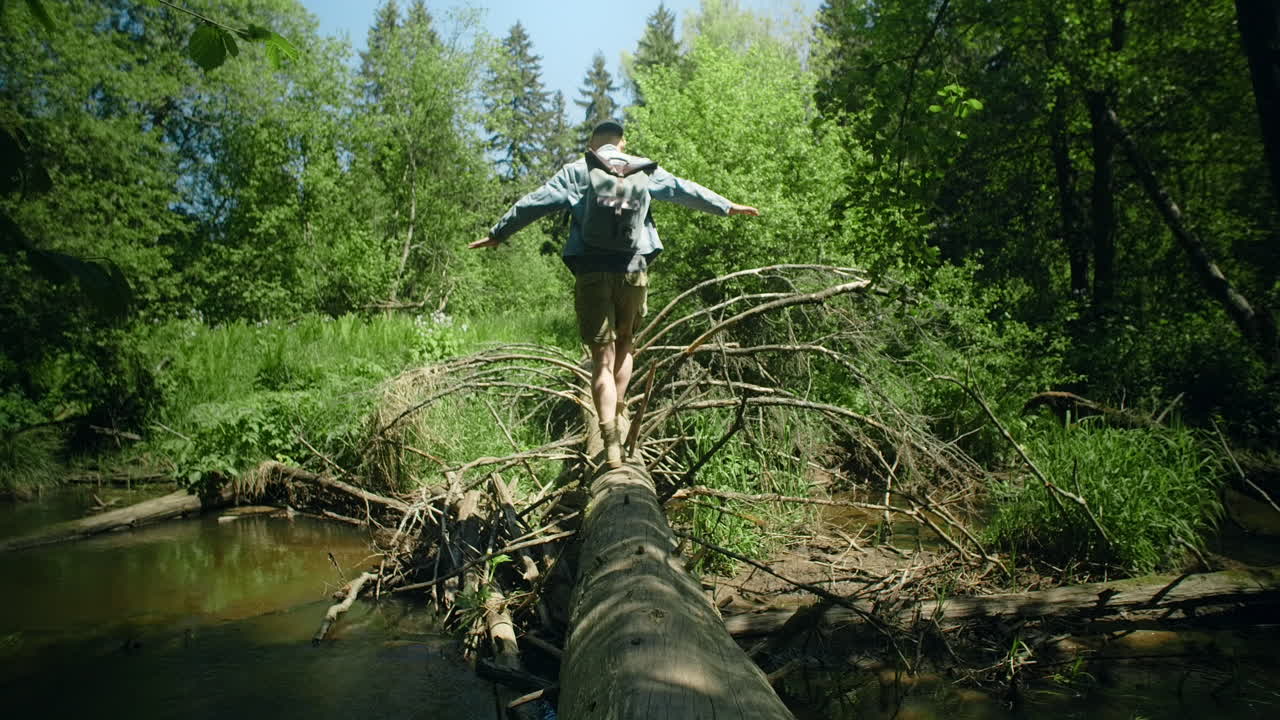 Man Balances Across Fallen Log in Forest Stream