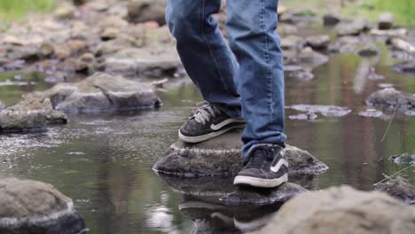 water insects skitter on small, slow stream then boy’s feet jump on rocks to cross the water