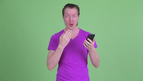 fotografía de estudio de un joven recibiendo grandes noticias mientras usaba el teléfono contra un fondo verde