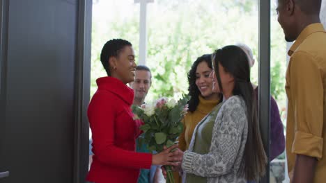 happy diverse friends arriving and hugging at the front door of house for christmas dinner table