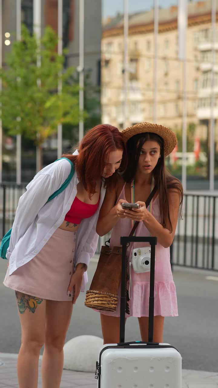 dos mujeres jóvenes mirando un teléfono cerca de una maleta