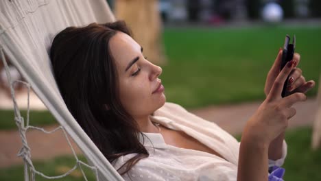 close up of a woman lying in a hammock outdoors, surfing internet on tablet, clicks on the screen