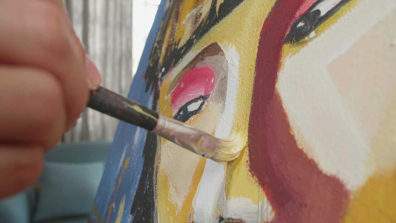 cerca de una mano sosteniendo un pincel de colores mixtos y pintando la nariz de una niña en el lienzo