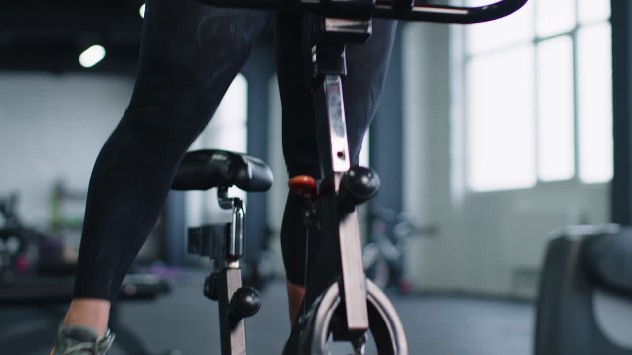 Portrait caucasian woman exercising workout on stationary cycling machine bike in gym slow motion