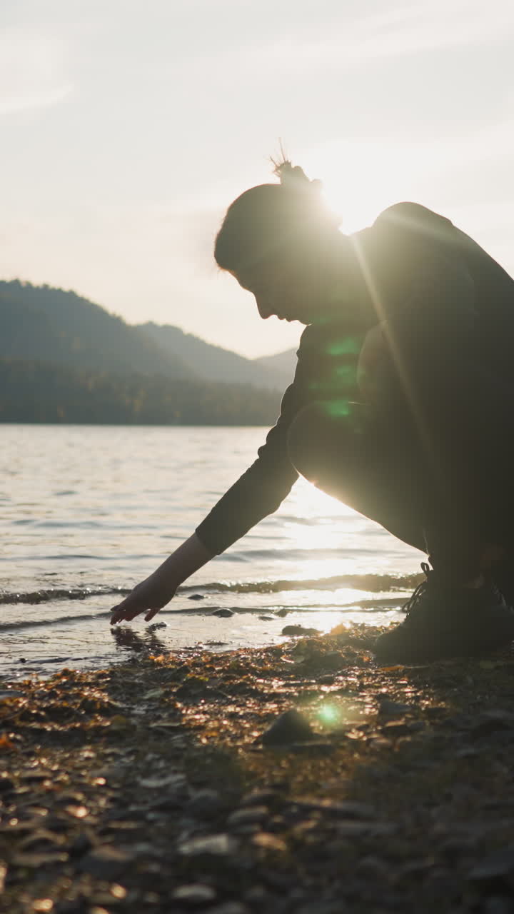 한 여인이 해가 지면 호수 안으로 손가락을 넣고, 한 여인이 혼자 물 에 앉아 가을 저녁에 평온한 자연을 발견하고, 고독을 즐기기 위해 완벽한 순간.