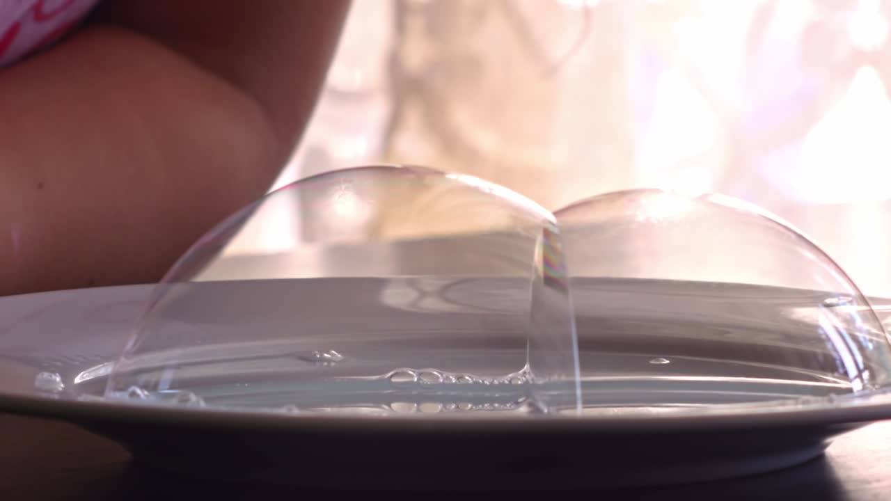 科学実験のクローズアップ。ストローで石鹸液に空気を吹き込み、表面に半透明の泡ができる様子。