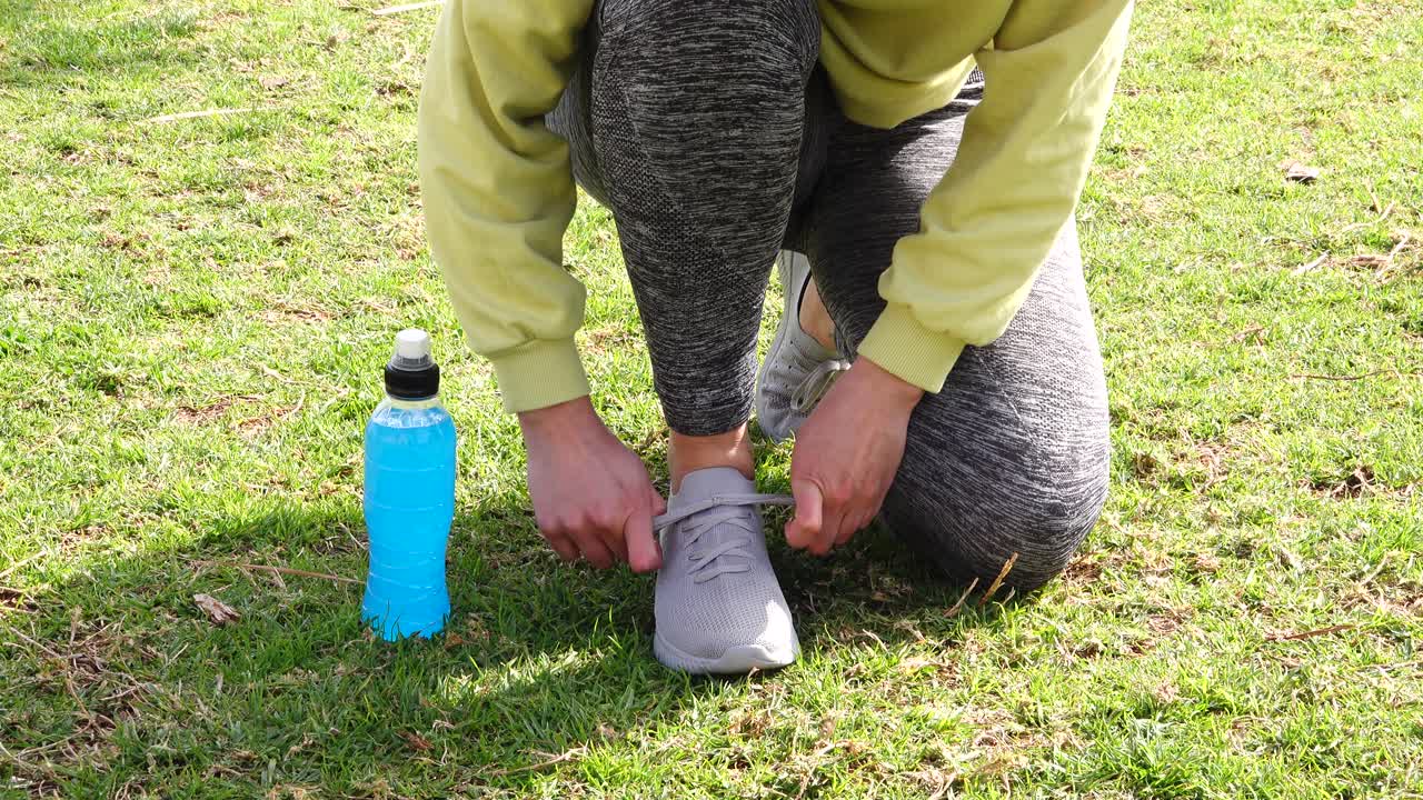 atleta che lega scarpe da ginnastica sull'erba con bevanda isotonica blu accanto