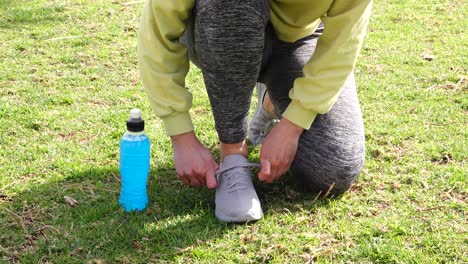 Atleta-Atando-Zapatillas-De-Deporte-En-La-Hierba-Con-Una-Bebida-Isotónica-Azul-Al-Lado