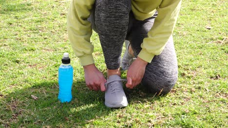 athlete tying sneakers on grass with blue isotonic drink beside