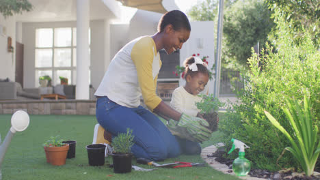 happy african american mother and daughter gardening, planting plants in garden