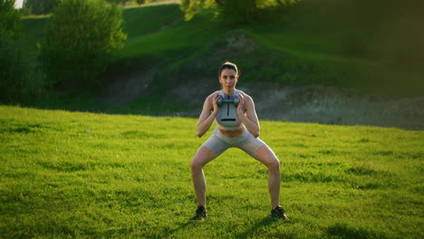 a woman squats with dumbbells in the park at sunset performing lunges to the side. motivation and sports training. a single woman does exercises at sunset in the summer